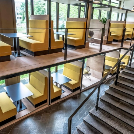 Moderne kantoorruimte in Meppel met meerdere werkplekken in gele cabines op twee niveaus, ideaal voor een creatieve werkomgeving. Grote ramen laten veel natuurlijk licht binnen.