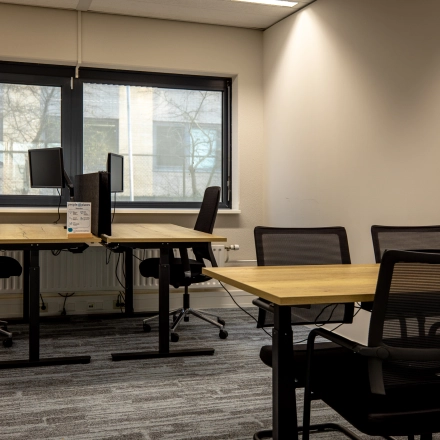 Kantoorruimte huren bij Gooimeer 1, Naarden: moderne werkplekken met houten bureaus en ergonomische stoelen, ideaal voor productief werk. Grote ramen zorgen voor natuurlijk licht.