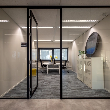 Moderne kantoorruimte huren in Naarden met glazen wanden, voorzien van bureaus en stoelen, gelegen aan Gooimeer 1.