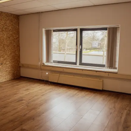 Lege kantoorruimte met houten vloer en groot raam met uitzicht op de straat, in een kantoorpand aan de Abdis van Thornstraat 74 in Oosterhout Nb.