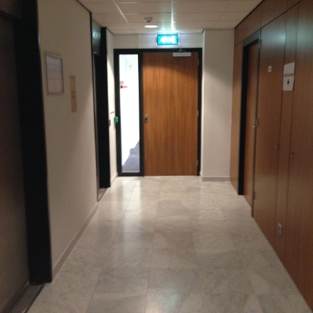 Een smalle gang in een kantoorpand op JC van Markenlaan 3, Rijswijk, met marmeren vloer en houten deuren. Ideaal voor kantoorruimte huren.