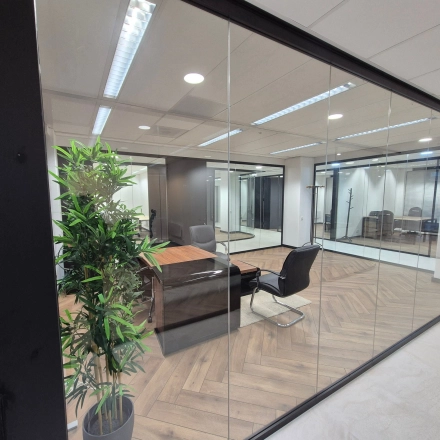 Kantoorruimte huren op JC van Markenlaan 3 in Rijswijk met moderne glazen wanden, houten vloer en twee stoelen rond een houten tafel. De ruimte is stijlvol verlicht en beschikbaar als kantoorpand.