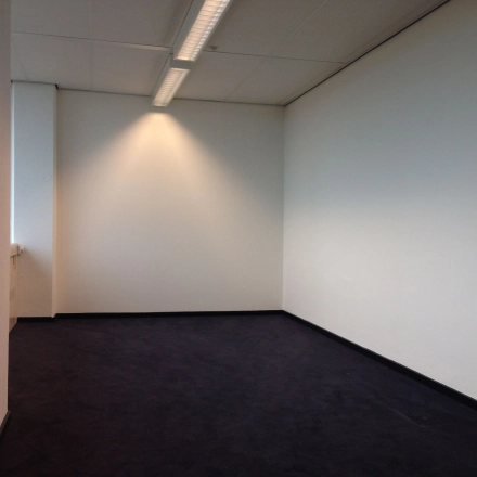 Lichte kantoorruimte te huur aan J.C. van Markenlaan 3 in Rijswijk met witte muren en een donker tapijt, ideaal voor creatieve inrichtingen.