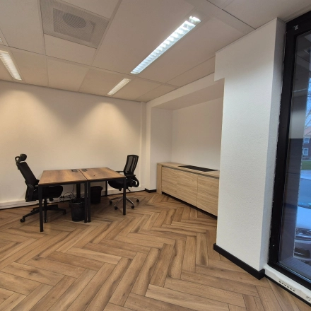 Moderne kantoorruimte te huur aan JC van Markenlaan 3 in Rijswijk met houten vloeren en twee bureaus naast grote ramen die natuurlijk licht binnenlaten.