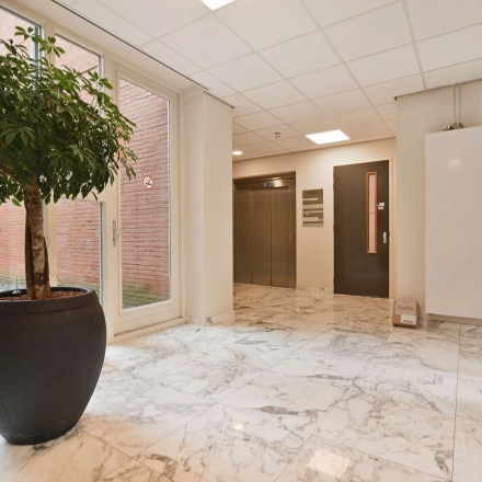 Entree van een kantoorpand aan de Laan van Vredenoord 17-19 in Rijswijk, met marmeren vloer en een grote plant naast de lift. Ideaal voor kantoorruimte huren.