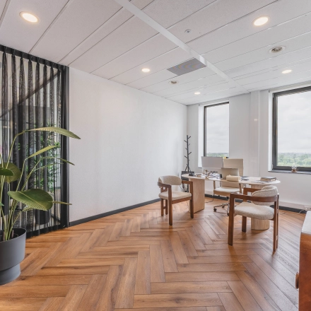 Ruime kantoorruimte met houten vloer en grote ramen in Rijswijk, geschikt om te huren voor zakelijk gebruik. Voorzien van twee bureaus en comfortabele stoelen.