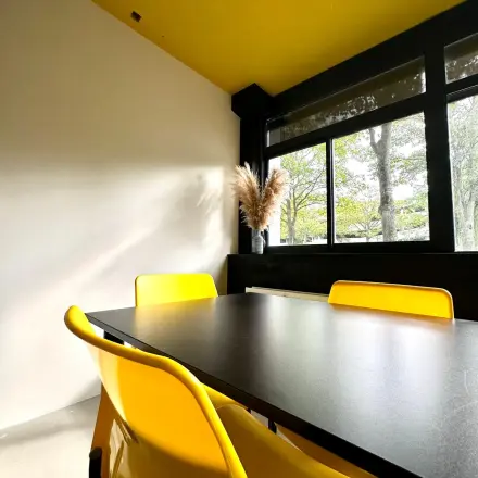 Moderne kantoorruimte huren op Volmerlaan 7 in Rijswijk met een uitnodigende vergadertafel en opvallende gele stoelen, met uitzicht op groen buiten. Perfect voor creatieve brainstormsessies.