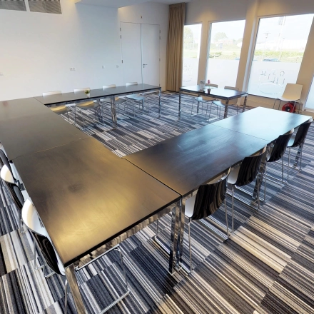 U-vormige vergaderruimte in Roermond met stijlvolle bureaus en stoelen, grote ramen zorgen voor veel natuurlijk licht. Kantoorruimte huren op Boven de Wolfskuil 3 biedt een moderne setting voor zakelijke bijeenkomsten.