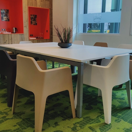 Een moderne kantooruimte met een lange tafel omringd door stoelen in een kleurrijke setting op Boven de Wolfskuil 3, Roermond, geschikt voor vergaderingen of als werkplek te huur.
