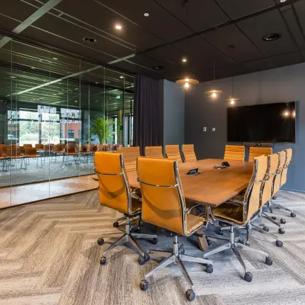 Moderne vergaderruimte in een kantoorpand aan de George Hintzenweg 77-89 in Rotterdam Alexander, met stijlvolle bruine leren stoelen en een groot houten tafelblad, ideaal om kantoorruimte te huren.