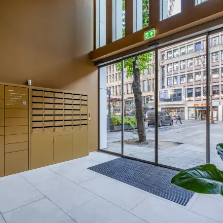 Ingang van kantoorpand aan het Stadhuisplein 9-23 in Rotterdam Centrum met grote ramen en een pakketkast.