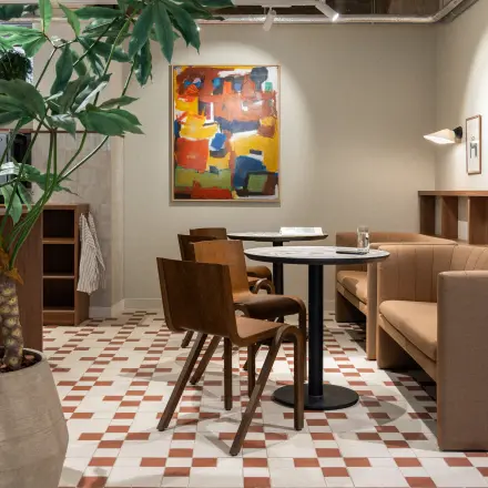 Moderne kantoorruimte in Rotterdam Centrum met gezellige zithoek, hoog plafond, kleurrijk schilderij en stijlvolle meubels. Ideale plek voor informeel overleg of ontspannen pauze.