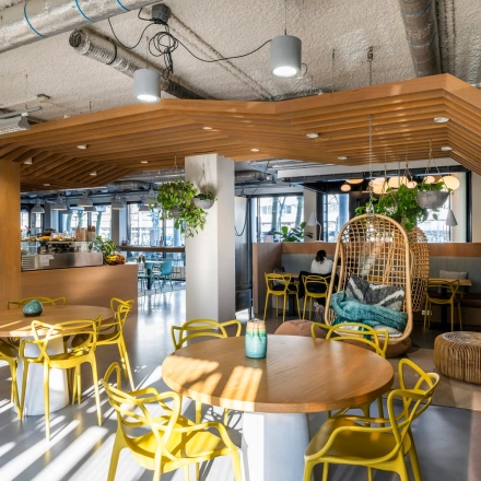 Moderne en lichte kantoorruimte met houten en gele accenten, ideaal voor informele bijeenkomsten en ontspannen werkmomenten op Westblaak 180 in Rotterdam Centrum. Planten en stijlvolle lampen geven de ruimte een frisse uitstraling.