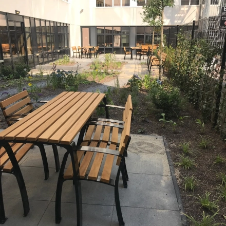 Buitenruimte van een kantoorpand met houten tafels en banken, omlijst door groen, gelegen op Westblaak 180 in Rotterdam Centrum.