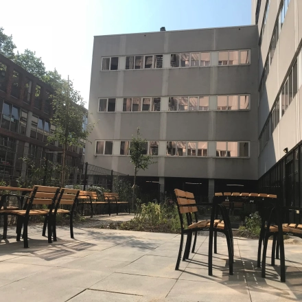 Buitenaanzicht van kantoorpand Westblaak 180 in Rotterdam Centrum, met moderne architectuur en betegeld terras met houten tafels en stoelen.
