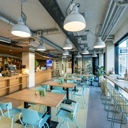 Moderne en lichte kantoorruimte op Westblaak 180 in Rotterdam Centrum, geschikt voor verhuur. De ruimte heeft een open indeling met houten tafels en blauwe stoelen neergezet in een café-achtige opstelling.