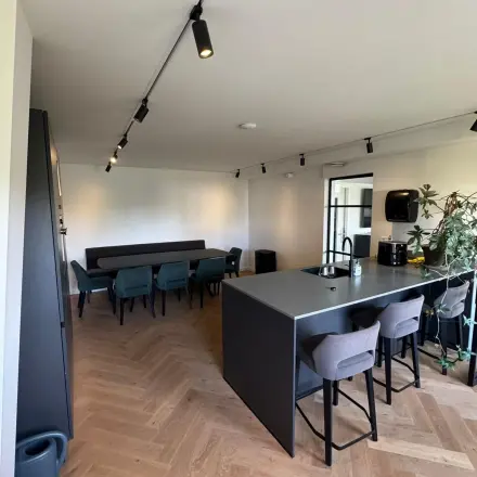 Moderne kantoorruimte in Rotterdam Centrum met houten vloer, stijlvolle bar met krukken en lange houten tafel met stoelen. Veel natuurlijk licht en groene planten voor frisse uitstraling.