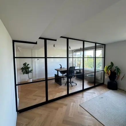 Moderne kantoorruimte met houten vloer en glazen wanden, uitgerust met een bureau en planten. Ideaal voor wie een kantoorpand wil huren in Rotterdam Centrum.