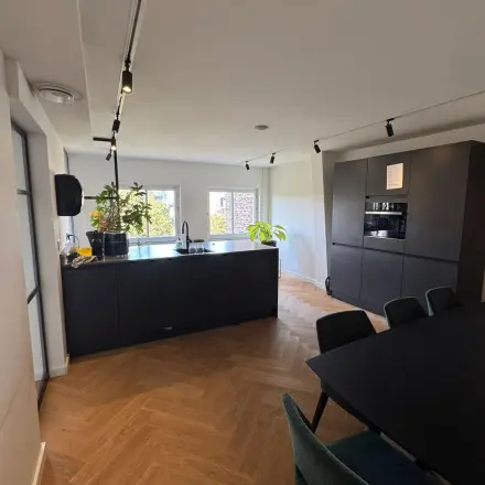 Moderne keuken in kantoorpand op Westplein 12, Rotterdam Centrum, met houten vloer, zwarte kasten en een ruime eettafel. Lichte ruimte met veel planten, geschikt voor vergaderingen of informele ontmoetingen.