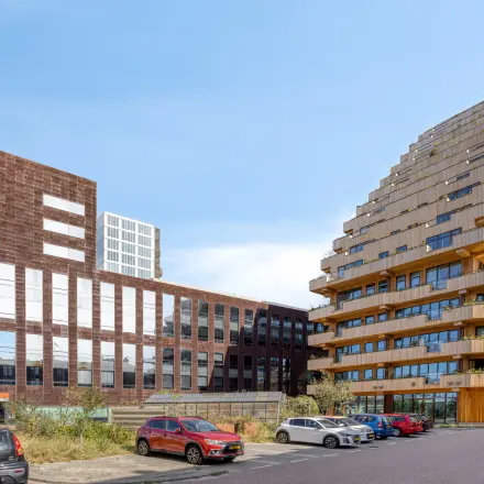 Moderne kantoorpand aan de Kratonkade 7-27 in Rotterdam Delfshaven, omgeven door andere eigentijdse gebouwen en met een ruime parkeerplaats ervoor.