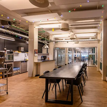 Kantoorruimte huren op Kratonkade 7-27 in Rotterdam Delfshaven met lange tafel, stoelen, moderne keukenfaciliteiten en kleurrijke verlichting. Ideaal voor samenwerking en creatieve projecten.
