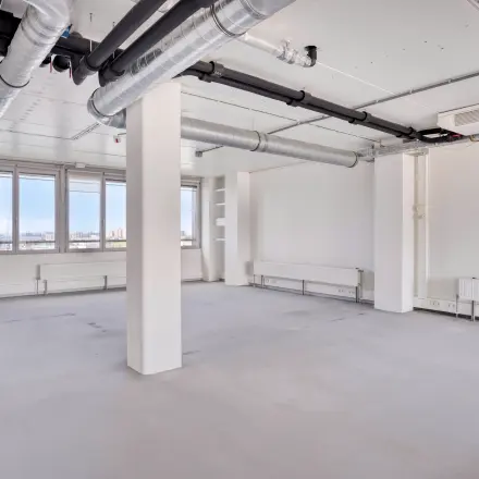 Lichte kantoorruimte op Kratonkade 7 - 27 in Rotterdam Delfshaven, met witte muren, buizen aan het plafond en grote ramen. Ideaal voor kantoorruimte huren.