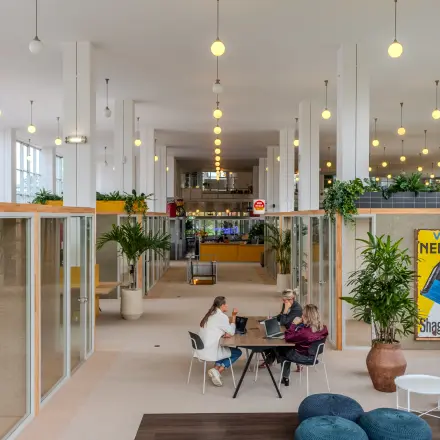 Kantoorruimte huren op Van Nelleweg 1 in Rotterdam Delfshaven met moderne werkplekken, veel licht en planten. Vier personen aan een tafel voeren zakelijke activiteiten uit in een ruim kantoorpand.