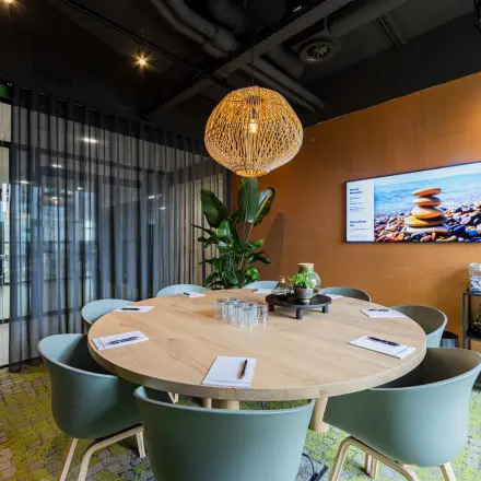 Een moderne vergaderruimte in een kantoorpand op Wilhelminaplein 1-40, Rotterdam Kop van Zuid, met een ronde tafel, stoelen en een scherm aan de muur.