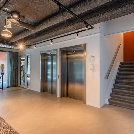 Een moderne kantoorruimte met liftlobby in het kantoorpand aan de Waalhaven O.z. 85, Rotterdam Waalhaven. Twee liften en een trap naast een zithoek met uitzicht op andere kantoren.