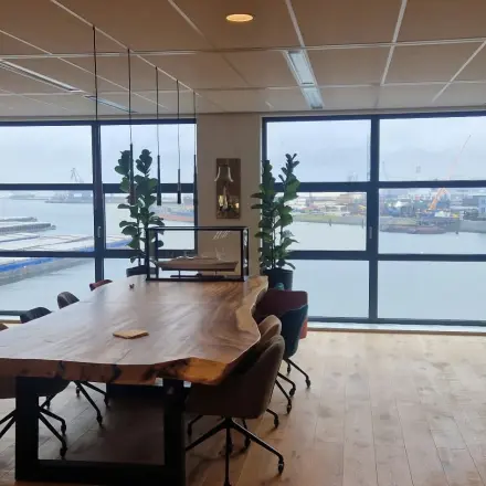 Vergaderruimte met houten tafel en stoelen, grote ramen met uitzicht op de haven, geschikt voor kantoorruimte huren in Rotterdam Waalhaven.