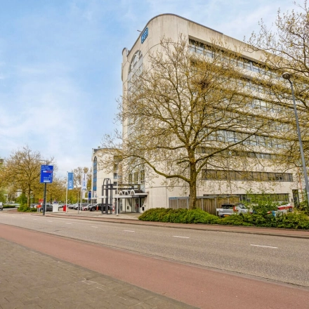 Buitenaanzicht van kantoorpand aan de Brauwweg 52-66 in Schiedam, met moderne architectuur omgeven door bomen en geparkeerde auto's.