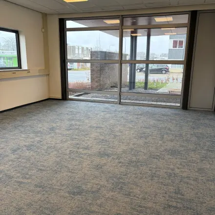 Lege kantoorruimte met grote ramen en blauw tapijt op Fischerpad 106, Sittard, beschikbaar om te huren.