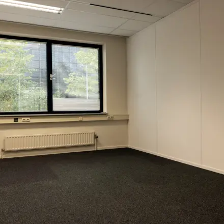 Leeg kantoor op Curieweg 9 in Spijkenisse, met grijze vloerbedekking en groot raam, ideaal voor uw kantoorruimte huren.