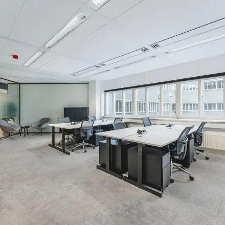 Lichte en moderne kantoorruimte met uitzicht op een gebouw, voorzien van bureaus en stoelen op Leidseveer 2-10, Utrecht Centraal Station, ideaal om te huren.
