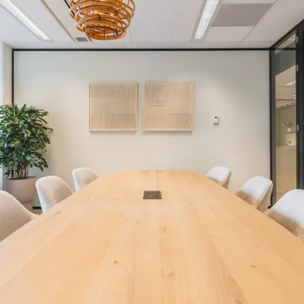 Vergaderruimte in een kantoorpand in Utrecht Centraal Station met houten tafel, comfortabele stoelen en kunst aan de muren.