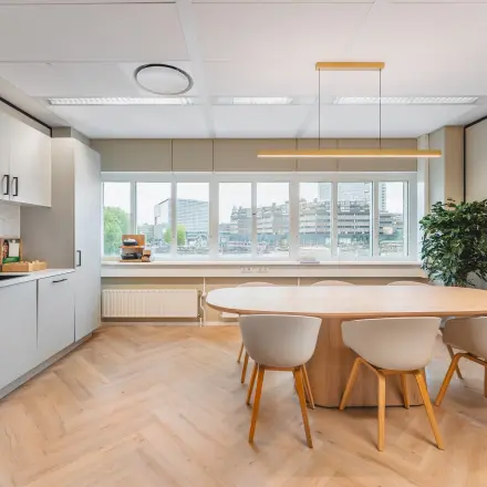Kantoorruimte met houten vloer en grote ramen bij Utrecht Centraal Station, gelegen op Leidseveer 2-10. De ruimte beschikt over een moderne tafel en keukenblok en biedt een aangename omgeving om te huren.