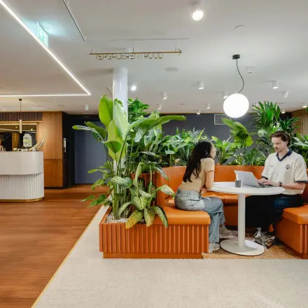 Sfeervolle kantoorruimte huren in Utrecht Centraal Station met moderne zitgelegenheid en groene planten. Twee mensen voeren een gesprek aan een tafel.