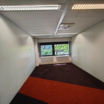 Leeg, goed verlichte kantoorruimte huren in kantoorpand op Bernadottelaan 13, Utrecht Kanaleneiland, met kleurrijke vloerbedekking en een groot raam voor natuurlijk licht.