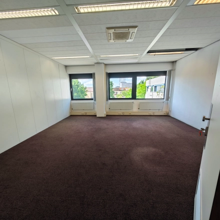 Een lege kantoorruimte op Bernadottelaan 13 in Utrecht Kanaleneiland, geschikt voor huur. Het pand heeft grote ramen die zorgen voor veel daglicht en een warme tapijtvloer.