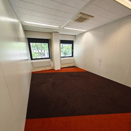 Lege kantoorruimte in Utrecht Kanaleneiland met tapijt, witte wanden en ramen die daglicht binnenlaten. Ideaal voor kantoren en verhuur aan bedrijven.