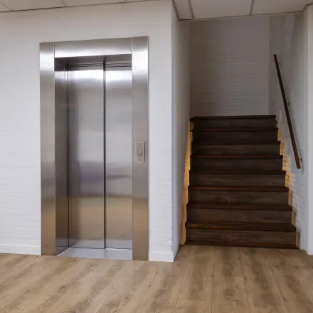 Entree van een kantoorpand met een lift en houten trap, geschikt voor kantoorruimte huren in Utrecht Lage Weide.