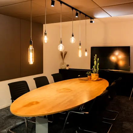 Vergaderruimte met een lange houten tafel, zwarte stoelen en sfeerverlichting, in een kantoorpand op Middenburcht 136, Utrecht Leidsche Rijn.