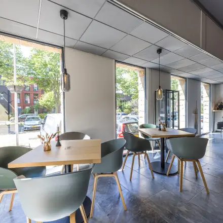 Lichte en moderne kantoorruimte aan de Goeman Borgesiuslaan 77 in Utrecht Noord, met tafels en stoelen nabij grote ramen. Ideaal voor werk of overleg. Gezellige huurkantooromgeving.