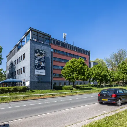 Exterieur van een kantoorpand te huur aan de Goeman Borgesiuslaan 77, Utrecht Noord. Brick facade met grote ramen omgeven door groene bomen en parkeerruimte langs de weg.