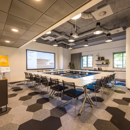 Vergaderruimte in kantoorpand op Goeman Borgesiuslaan 77, Utrecht Noord; moderne uitstraling met tafels, stoelen en projectiescherm. Ideale optie voor kantoorruimte huren.