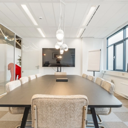 Vergaderruimte in kantoorpand op Daltonlaan 200, Utrecht Rijnsweerd met lange tafel, stoelen en groot scherm. Ideaal voor kantoorruimte huren.