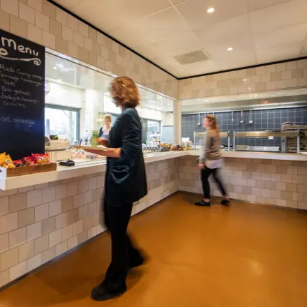 Een lichte pantry in een kantoorpand op Winthontlaan 200, Utrecht Zuid, met een vrouw achter een toonbank met snacks en een passerende persoon. Ideale plek voor kantoorruimte huren.