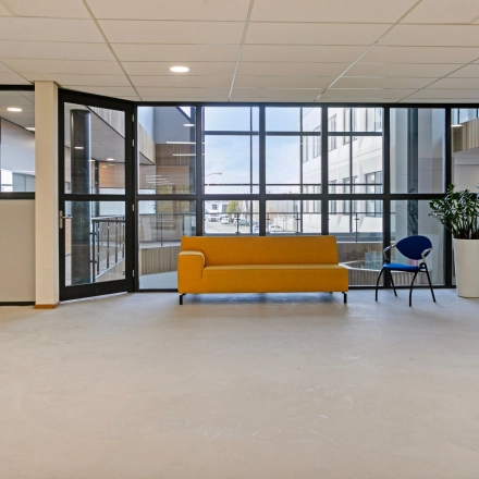 Grote open ruimte in het kantoorpand op De Run 4312, Veldhoven met glazen wanden, geel bankstel en interieurplanten. Ideaal voor kantoorruimte huren.
