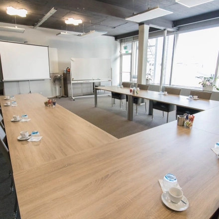 Vergaderruimte met grote tafel op Kaldenkerkerweg 20 in Venlo, ideaal voor kantoorruimte huren. De ruimte is voorzien van projectiescherm, whiteboard en comfortabele stoelen.