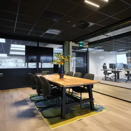 Modern ingerichte kantoorruimte met glazen wanden en houten tafel, gelegen op Havenweg 24 in Vianen Utr, ideaal om een kantoor te huren. Verschillende bureaus zijn zichtbaar door de glazen wanden.